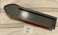 Large LEGO boat hull piece shown from above on striped fabric background with MaxSold lot number card, angled to show interior and shape.