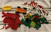 Photo of a pile of assorted small LEGO pieces including plates, bricks, wheels, and accessories in various colors on a fabric surface.