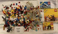 Photo of small mixed Lego pieces spread out on cloth surface with three Lego instruction booklets placed to the right.