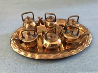 Six miniature brass kettles arranged on an oval brass tray showing their size, shape, and condition.