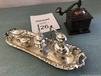 Photo of miniature silver toned tea set pieces on tray along with brass coffee grinder, showing ornate details and scale.
