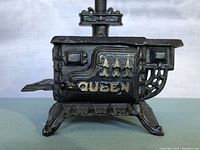 Front side view of the miniature cast iron stove showing the word 'QUEEN' on its side and decorative vent elements.