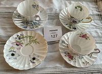 Three Shelley fine bone china tea cups sitting on three of the four scalloped saucers with floral designs.