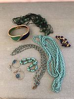 Full view of various teal and blue tone costume jewelry items spread out to show multiple necklaces, bracelets, and earrings.