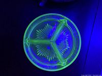 Top-down photo of the round uranium glass divided dish glowing green under UV/black light, showing the starburst pattern and three compartments.