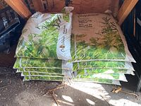Stack of 11 bags of Compliments Black Earth Topsoil in a shed, showing packaging and quantity.