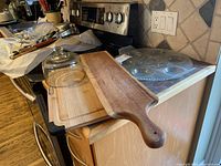 Wooden paddle cutting board, rectangular cutting board, and small glass cheese dome on kitchen counter