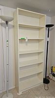 Front view of the six shelf white melamine bookcase between two standing lamps.