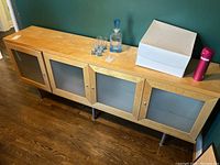 Full side view of the wooden cabinet with four frosted glass doors and metal legs, top surface showing some wear.