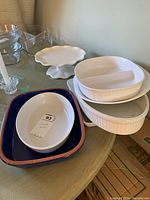 Various casserole dishes including Corning Ware, divided ceramic dishes, and glass bowls all stacked together on a table.