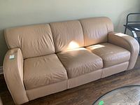 Front and top view of beige leather couch with three seat cushions and slightly indent on armrest.
