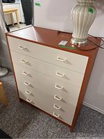 Front view of the dresser showing brown sides and top with white drawer fronts and white plastic handles, six drawers visible.