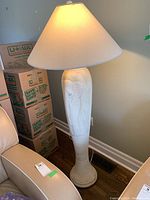 Full view of ceramic floor lamp with beige lampshade beside packed moving boxes and armchair.
