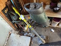 Yardworks electric garden shredder and hedge trimmer alongside Ryobi cordless lawn edger in a shed with visible dirt and wear.