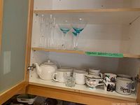 Shelf with assorted stemmed glassware, mugs, teapot, and cups.