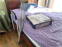 Photo showing crutches leaning on bed, box of toilet safety frame on bed, and bed guard rail beside mattress.
