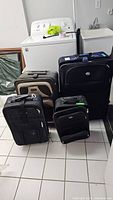 Four black luggage pieces of varying sizes arranged on tiled floor near washer and sink
