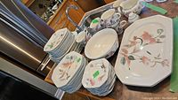 Full set of Mikasa dinnerware including plates, bowls, cups and platters with floral design stacked and laid out on table.