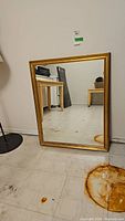 Photo of rectangular mirror with gold-tone frame leaning against wall, shows rust stains on mirror bottom and on floor.
