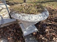 Side view of cement planter showing leaf pattern design and square base, planter contains dried grass and leaves.