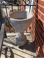 Front view of one cement pedestal planter, showing detailed floral and scroll designs on bowl and pedestal base