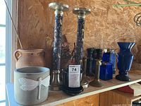 Shelf display of ceramic planters, blue glass vases, and various metal and glass candlesticks, showing diversity in size, color, and material.