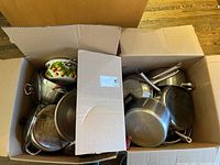 Two boxes filled with assorted pots and pans, some stainless steel, showing general use wear.