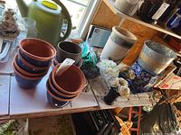 Nine plant pots stacked in two piles with navy blue bodies and terracotta rims, sitting on white surface near window.