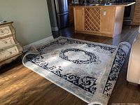 Area rug laid flat on a hardwood floor showing the central medallion and border design, with visible curling ends and stains.