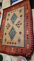 Image showing the geometric pattern rug with red border and beige center with blue and brown diamonds.