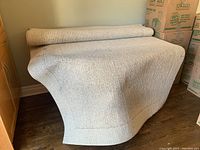 Area rug partially unrolled on hardwood floor with light beige color and subtle linear textured pattern.