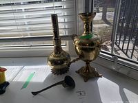 Brass metal samovar, vase, and ladle arranged on windowsill in natural light showing details of engraving and form.