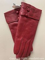 Pair of red women’s leather gloves laid flat showing front side with button details.