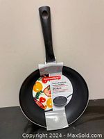 Front view of the frying pan showing the cooking surface, label attached around the handle and pan with slight wear on the side.