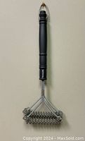 Single FSDUALWIN BBQ grill brush with black handle and coiled stainless steel spring head hanging on a wall hook.