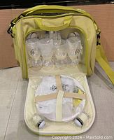 Front view of opened picnic bag showing stored cutlery items, wine glasses, plates, napkins and condiments.
