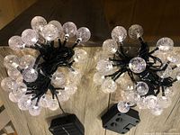 Two coiled sets of solar string lights showing clear bubble crystal ball bulbs on black wire with attached black solar panels.