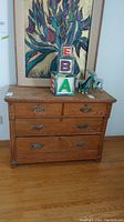 Front view of antique oak dresser with four drawers, two smaller top drawers with metal handles, and some items on top including decorative blocks and figurines.