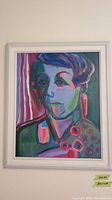 Full view of framed abstract portrait painting with colorful layered brushstrokes of a woman's face and red circular shapes, white wooden frame with some chips visible.