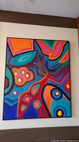 Full view of colorful abstract painting in black frame on wall.