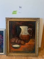 Front view of the original framed still life painting on board depicting a ceramic pitcher, bread, and dish.