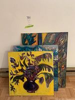 Three original unframed paintings on board stacked against wall showing colorful, abstract and impressionistic styles.