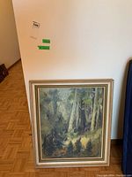 Full view of the framed painting leaning against a wall on a hardwood floor.