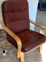 Brown leather tufted armchair with wooden frame shown from side angle with visible tufted buttons and curved wood armrests and legs.