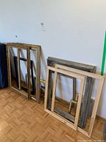 Photo showing assortment of wooden picture frames of various sizes and styles leaning against a wall on parquet flooring.