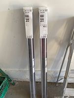 Two unopened IKEA TRETUR roller blinds in their original sealed plastic packaging, standing vertically against a wall in a garage space.