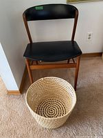 Chair front view showing teak frame and black vinyl seat and backrest, front right corner of the seat shows a small chip or damage.
