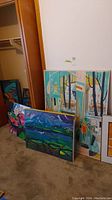Three framed canvas paintings leaning against wall