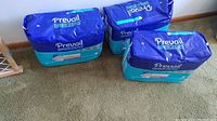 Three sealed packages of Prevail Breezers disposable underwear placed on a carpeted floor