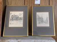 Two framed architectural prints with gray mats and gold-tone frames sitting on a wooden surface, one larger than the other.